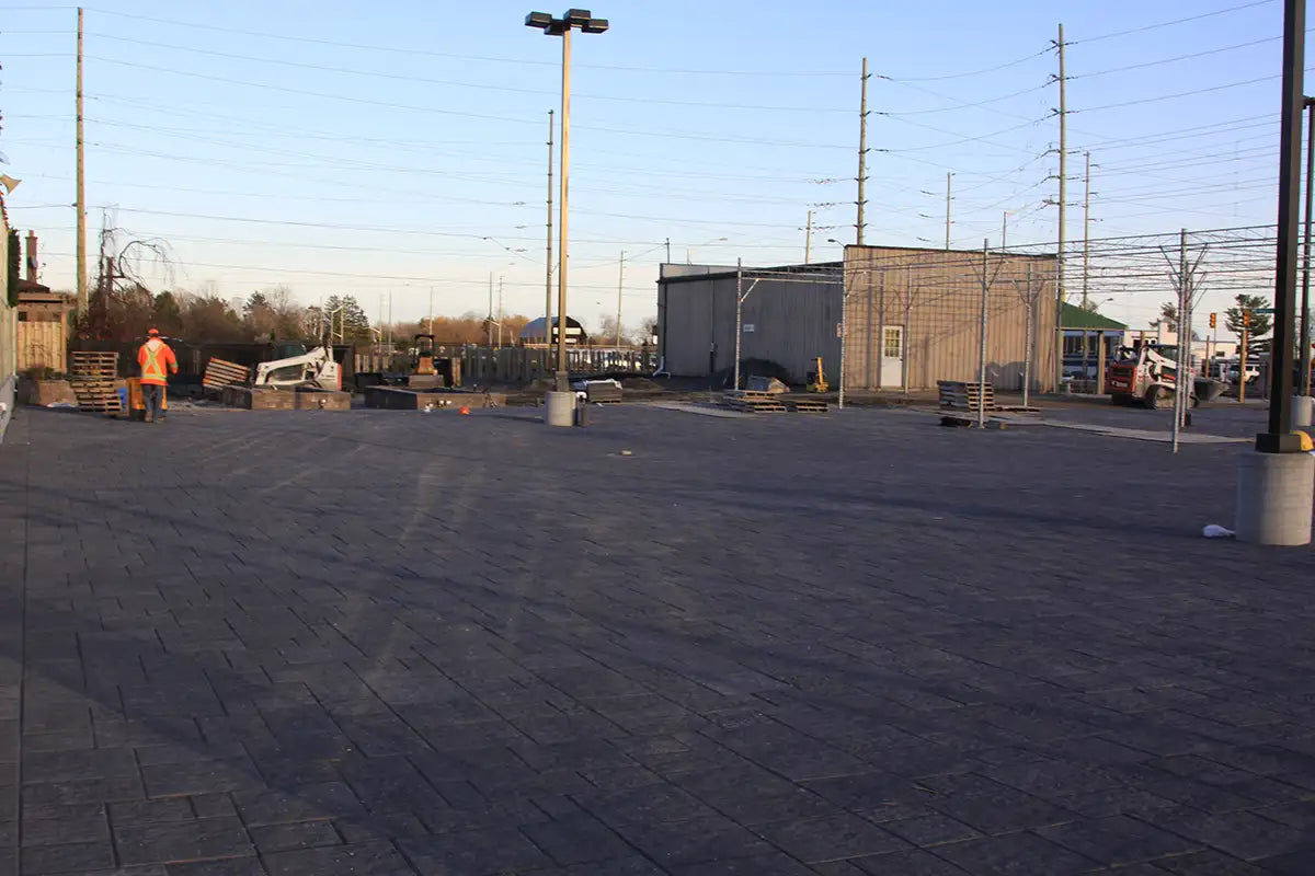 Fresh interlocked brick spanning yard with a person in an orange construction gear walking, and a few pieces of equipment
