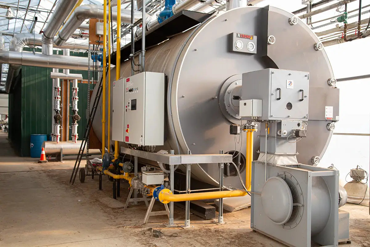 Large industrial boiler in the production greenhouse with pipes and equipment.