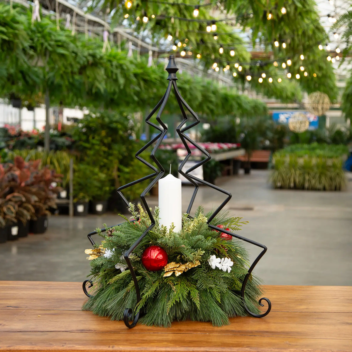 Decorative evergreen arrangement in black Christmas tree frame with pillar candle and decor.
