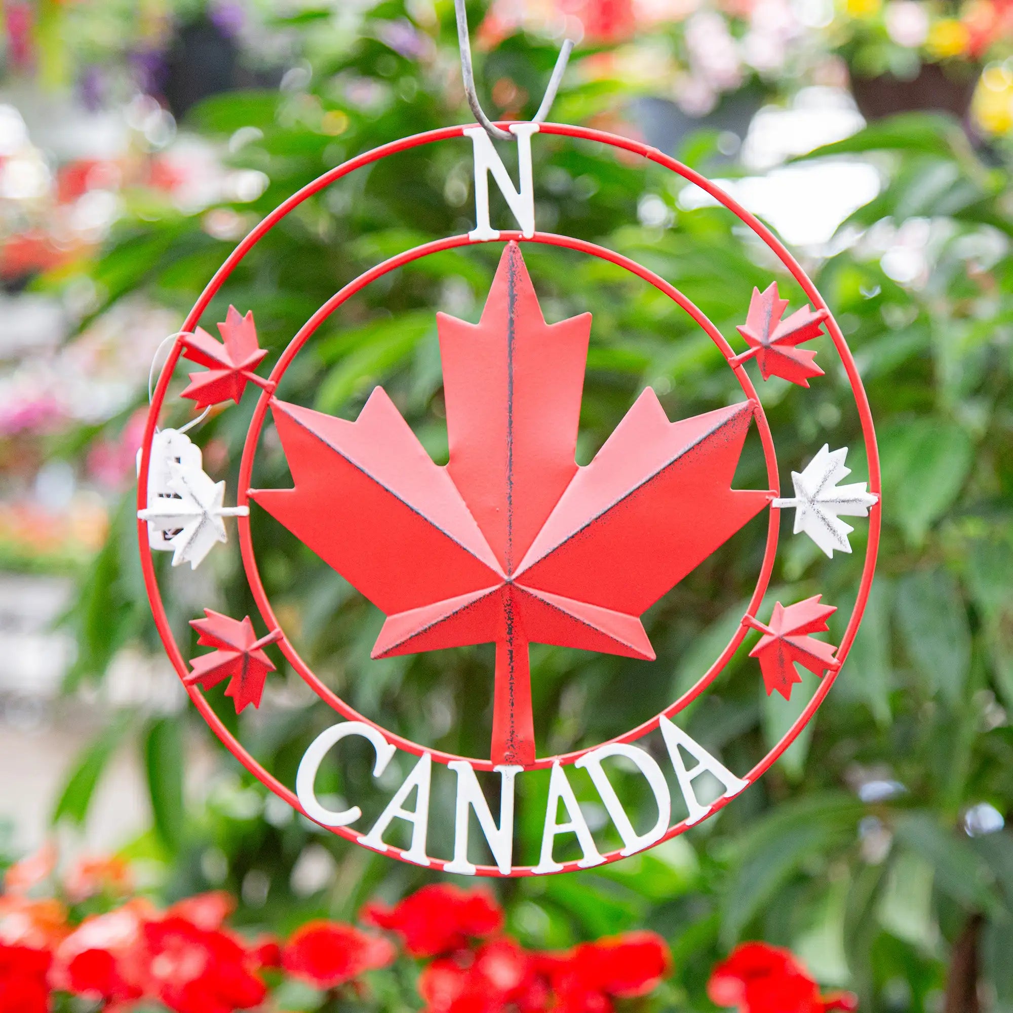 Decorative metal sign with red maple leaf and 'Canada' text, surrounded by greenery.