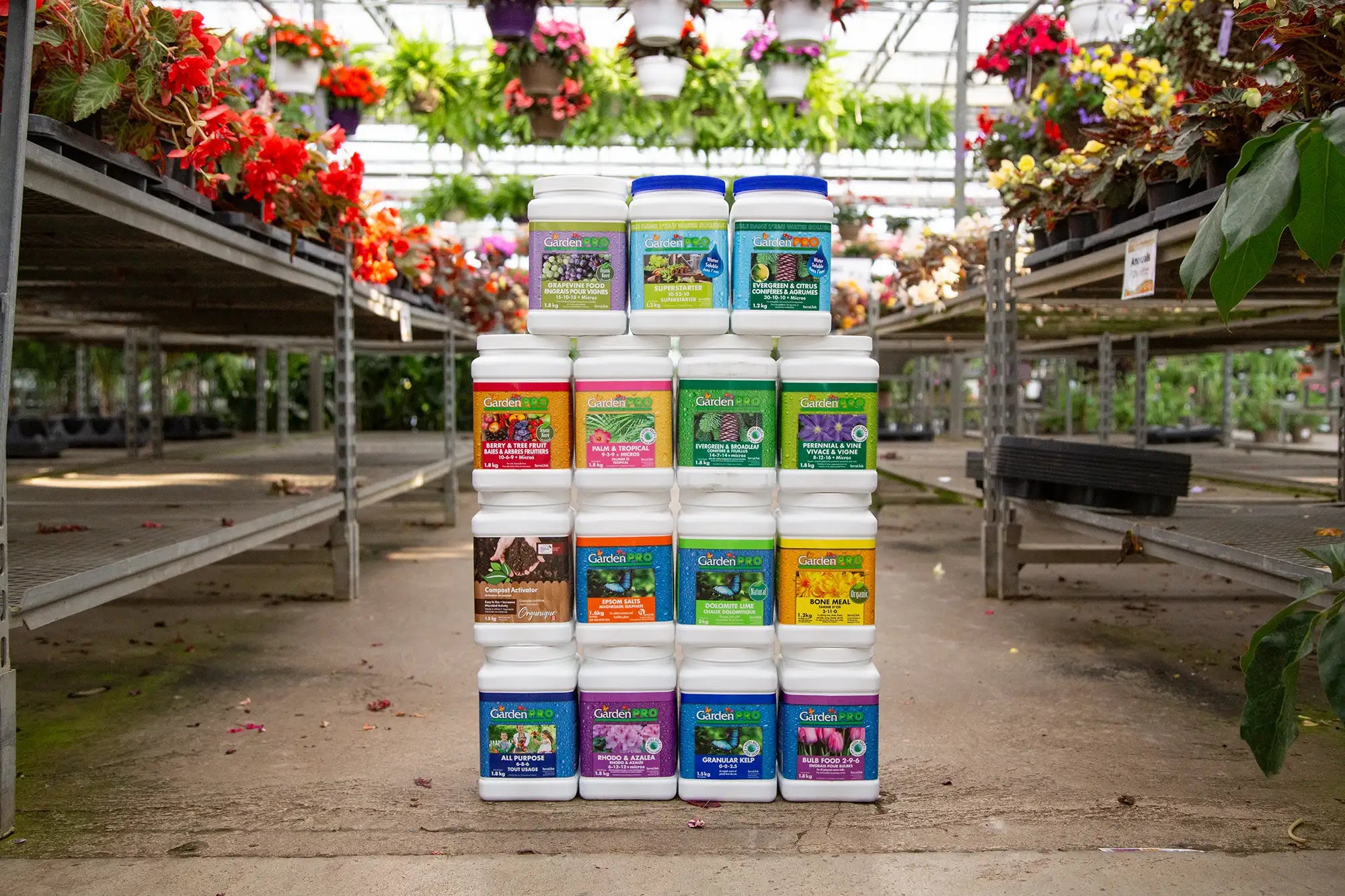 Stack of assorted Garden Pro fertilizer containers on concrete floor in a greenhouse setting