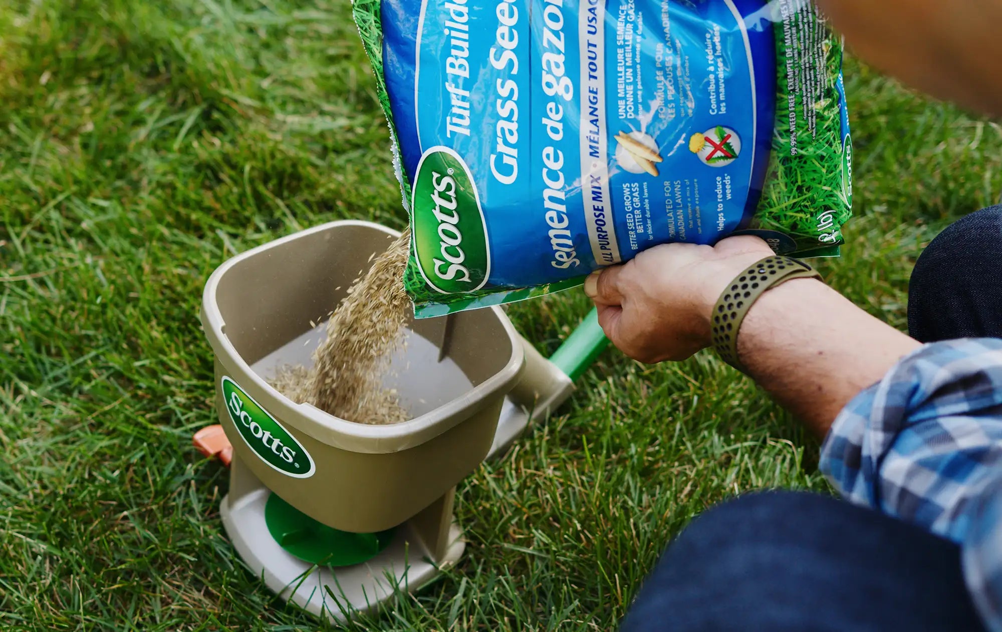 Person pouring Scotts grass seed into a spreader on grass
