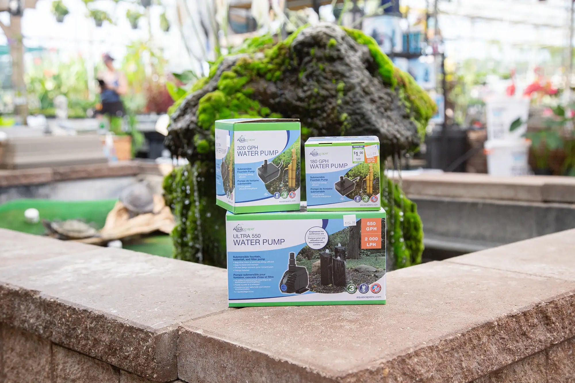 Three boxes of water pumps on a stone ledge with a pond feature in the background