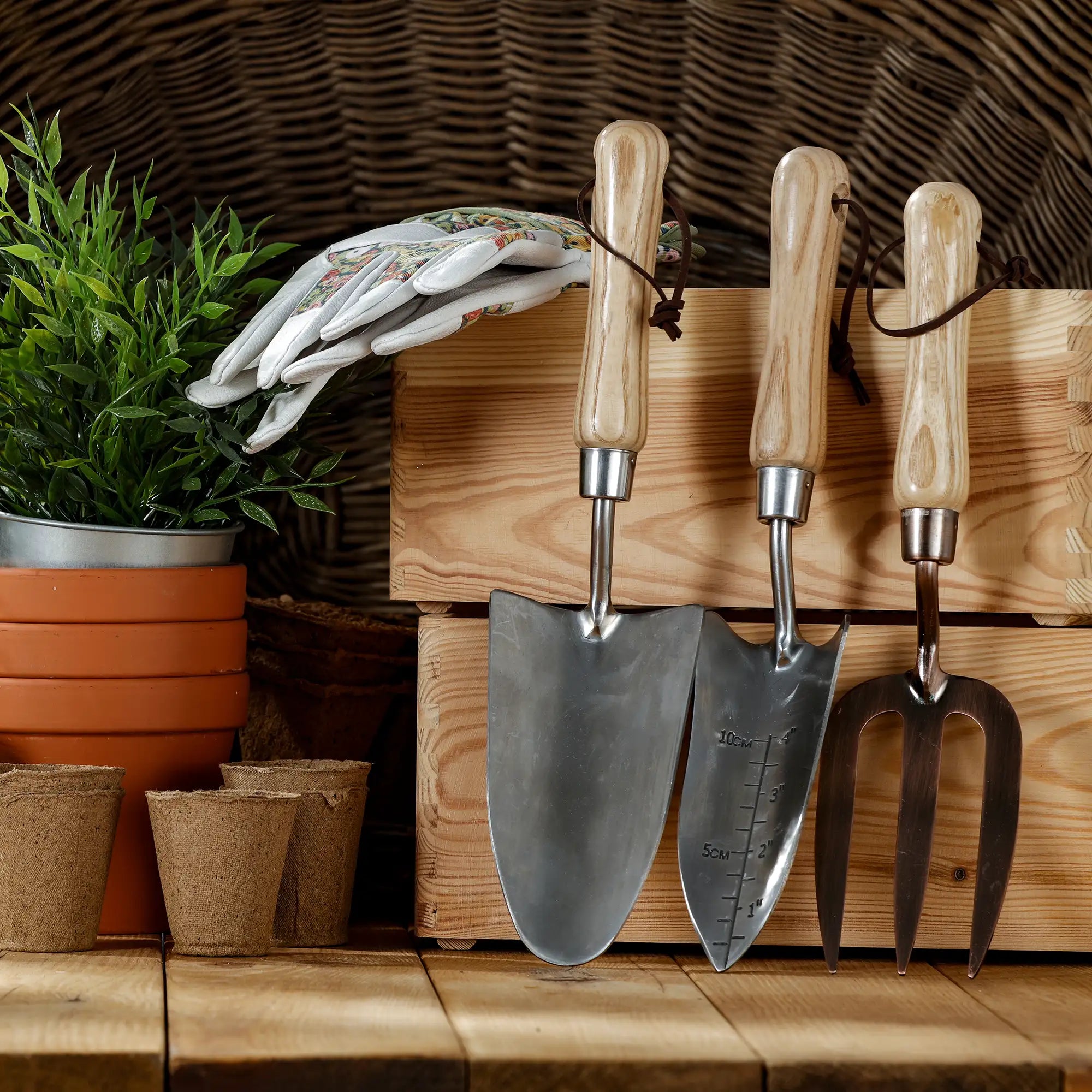 Collection of hand gardening tools including trowels and a fork on a wooden surface with plants and pots in the background.