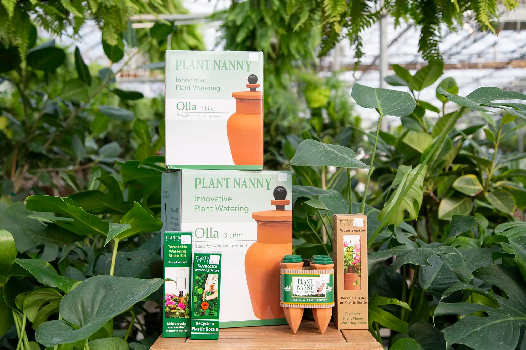 Product collection of Plant Nanny watering systems with green plants in the background.