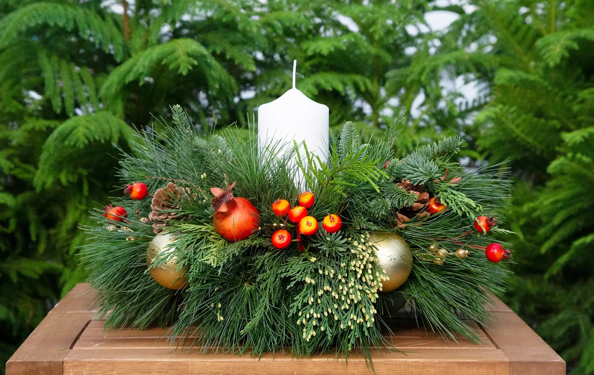 Decorative evergreen centrepiece with a white candle, dried fruit, and gold balls.