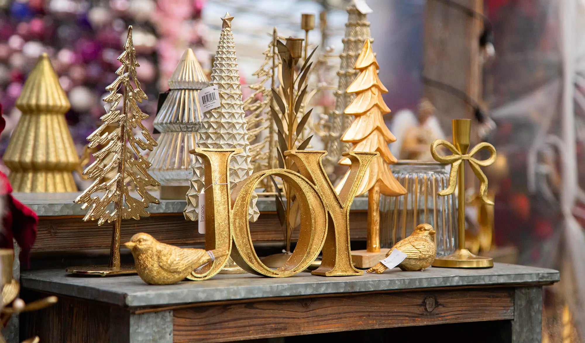 Decorative gold 'JOY' sign with metal Christmas trees and metal birds on a table.