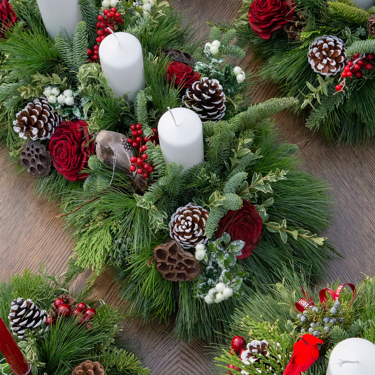 Flatlay top-down view of evergreen table centrepieces with white pillar candles, natural and red-themed elements
