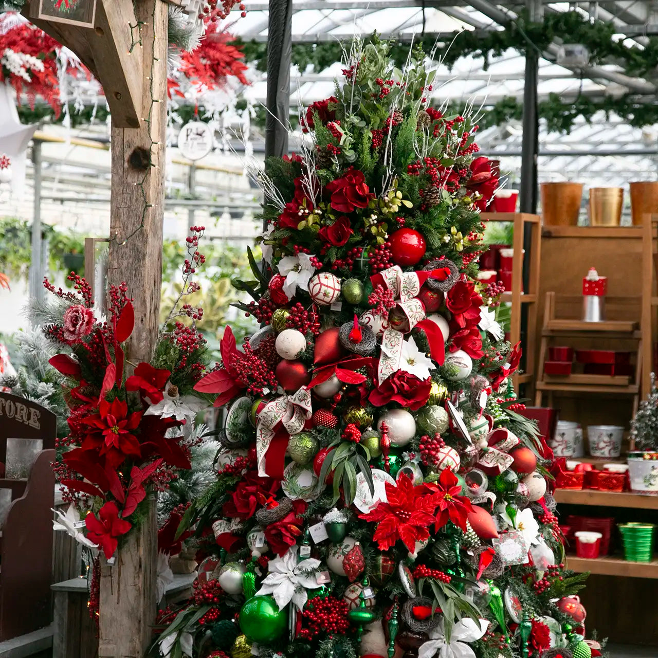 Decorated Christmas tree with red, green, and white ornaments in a greenhouse setting.