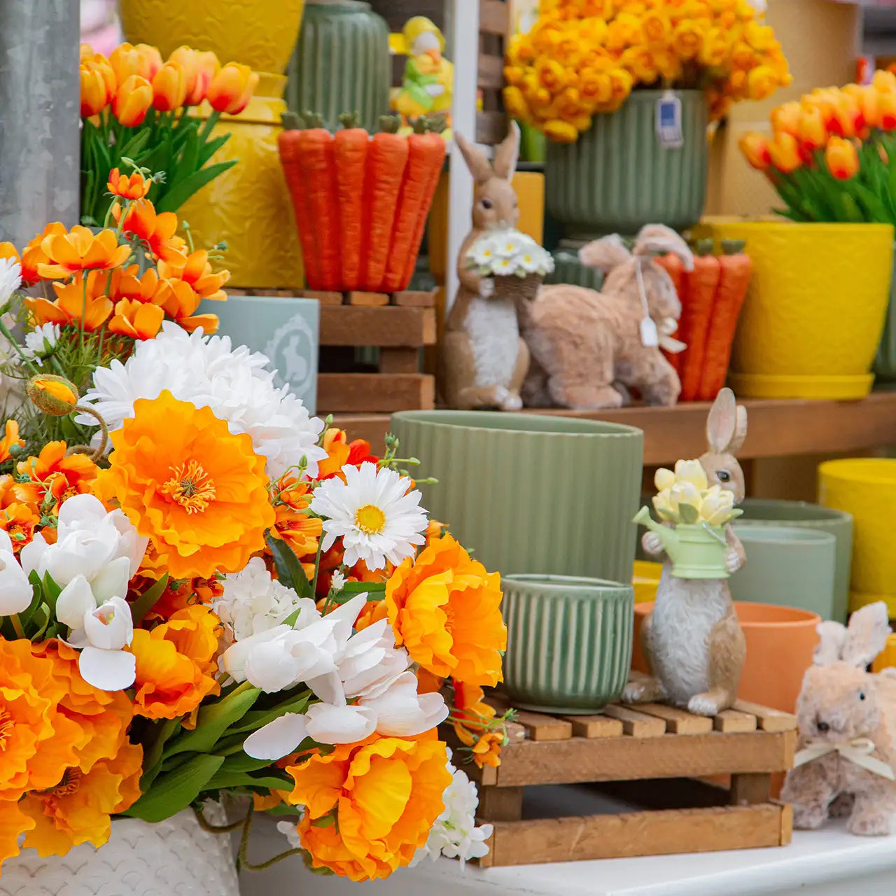 Faux florals in orange, yellow and white shades with display of Easter bunnies, carrots, and ceramic pottery.