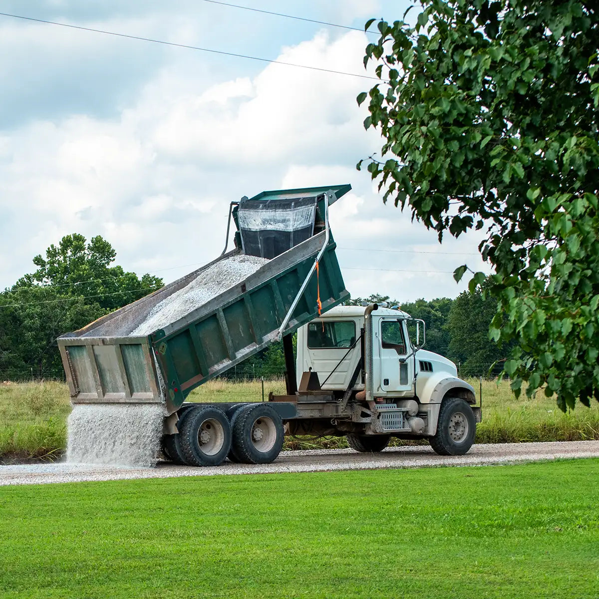 Dump truck unloading gravel on a driveway with trees in the background and foreground