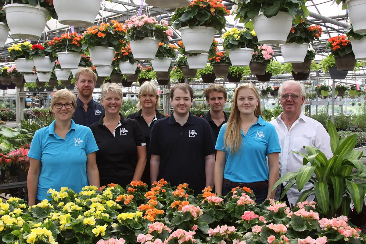 Vandermeer family posing in greenhouse with annuals on table and hanging baskets overhead. 