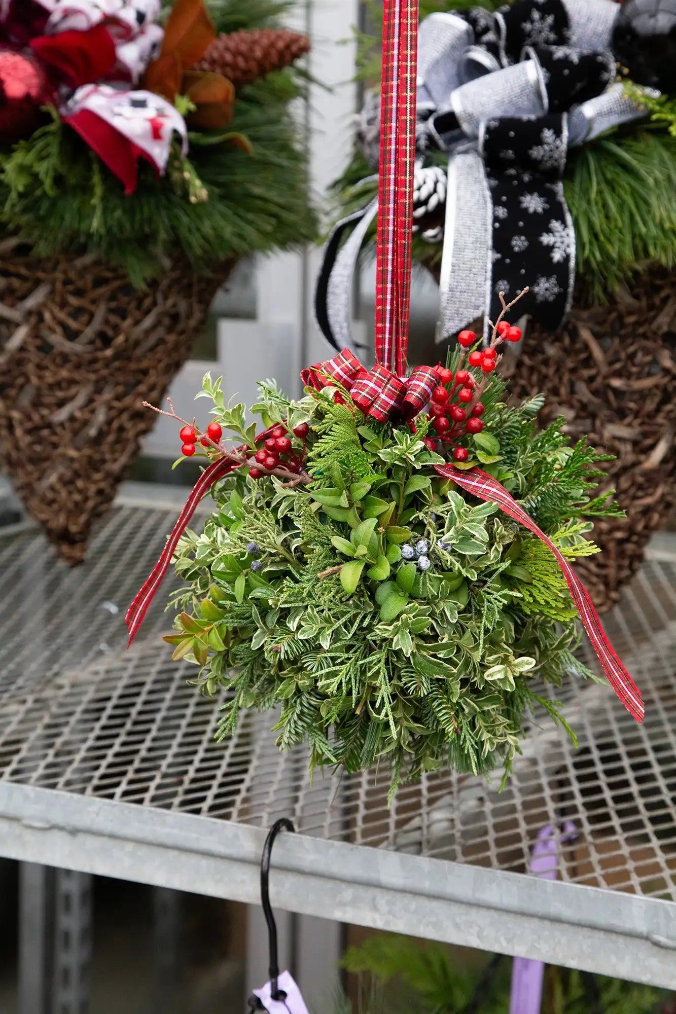 Hanging evergreen Christmas ball with mixed greenery, red berries, and ribbon.