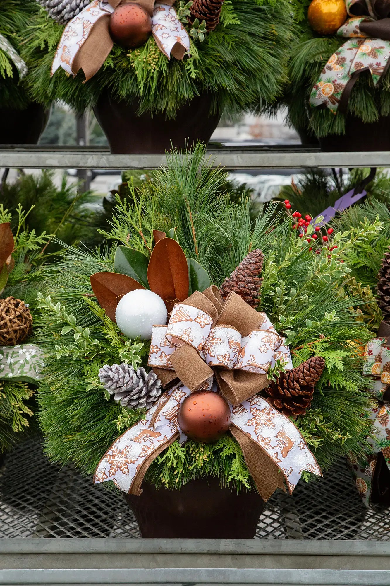 Decorative evergreen planter with greenery, ornaments, and gingerbread bow in an outdoor garden centre setting.