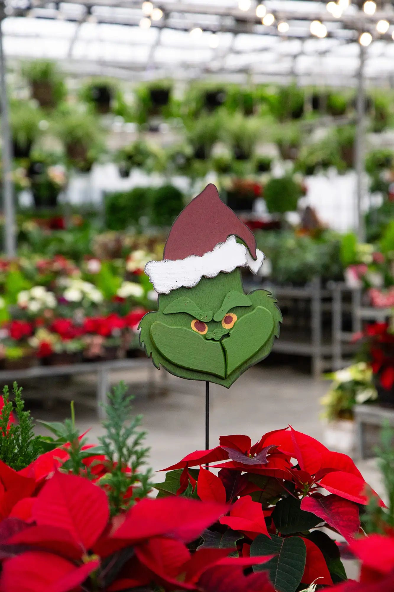 Decorative christmas decor shaped like the Grinch amidst potted plants in a greenhouse.