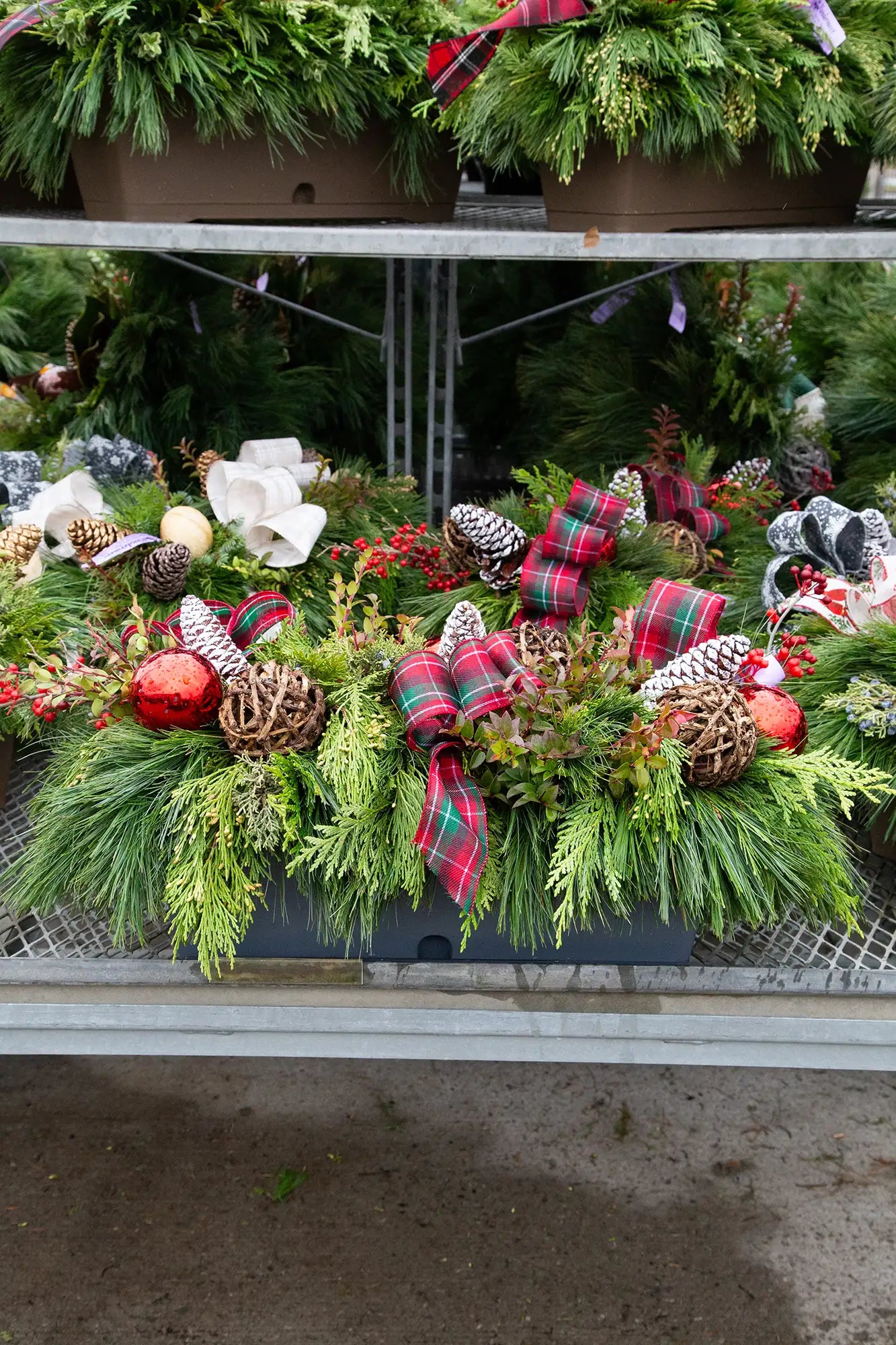 Decorative evergreen window box with greenery, ornaments, and plaid bow in an outdoor garden centre setting.