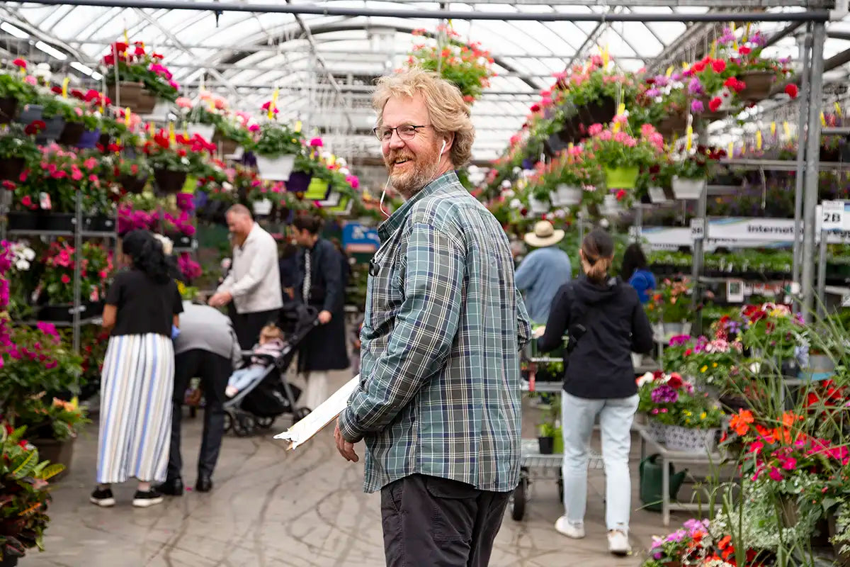 Staff member walking through a greenhouse filled with colourful annuals and people shopping.