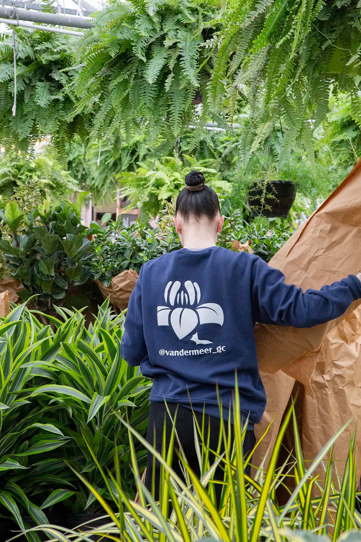 Staff member wearing a blue sweatshirt with Vandermeer logo on back, unpacking plants in a greenhouse.