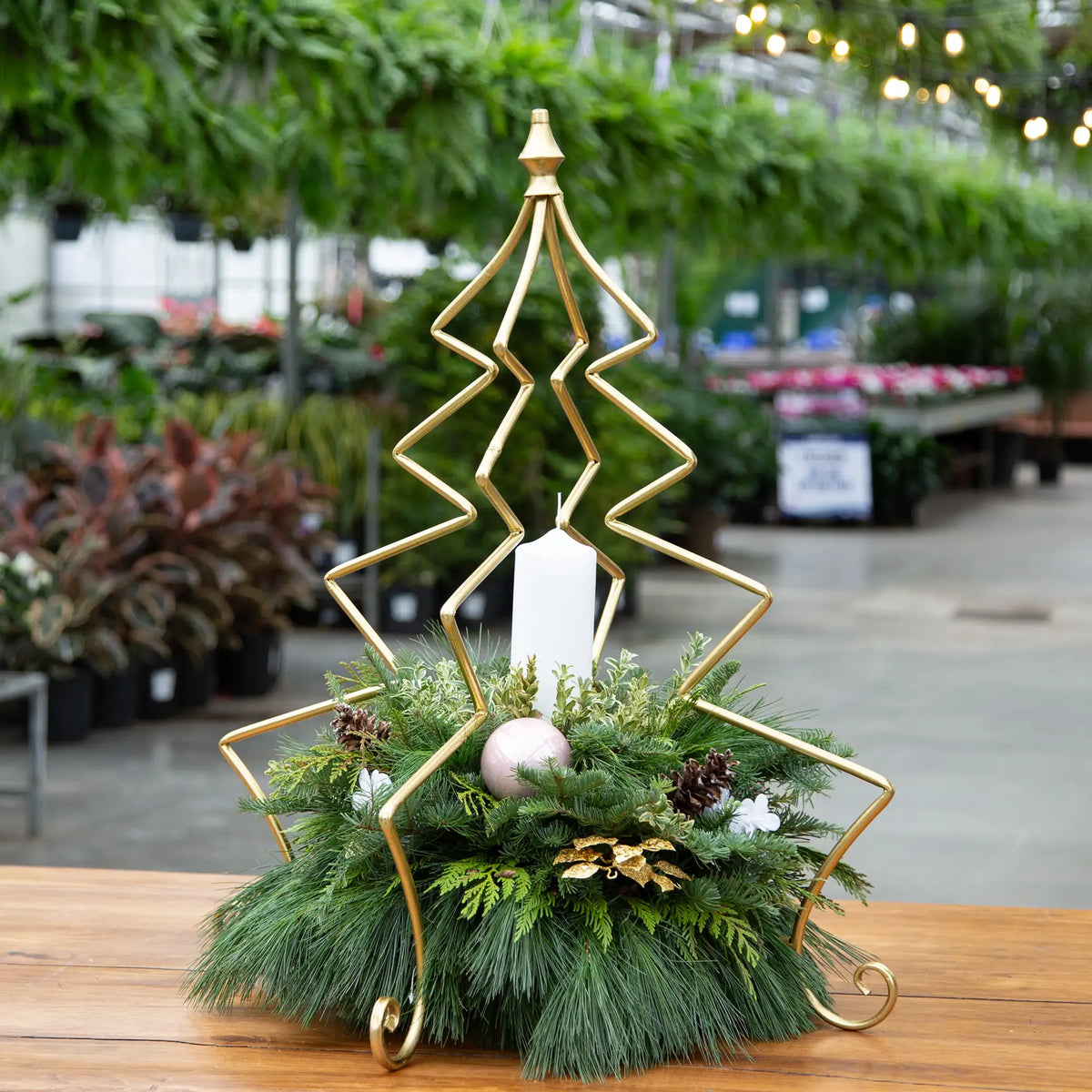 Decorative evergreen arrangement in gold Christmas tree frame with pillar candle and decor. 
