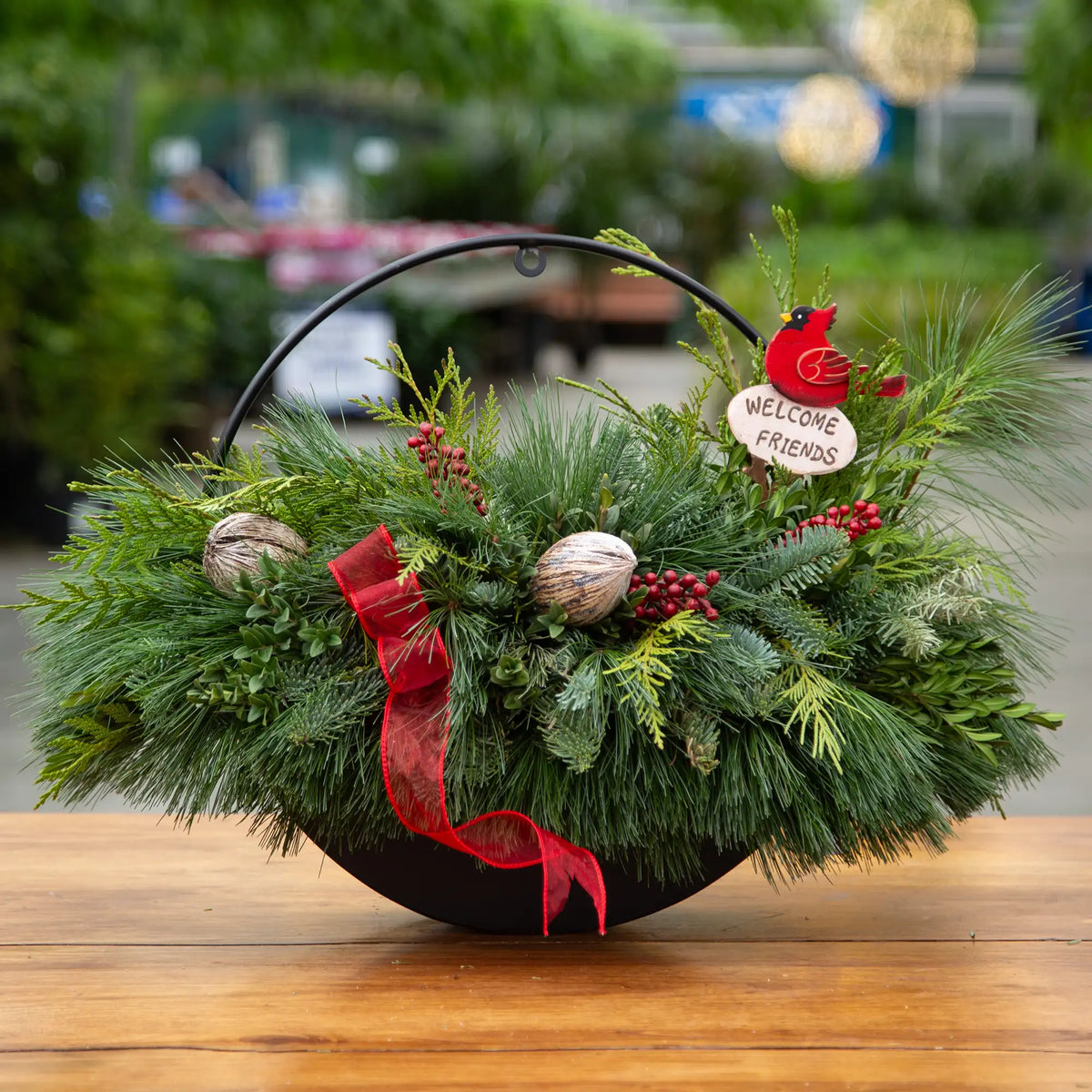 Black decorative round wall basket filled with evergreen arrangement, decor, a piece of ribbon, and wooden cardinal stake.
