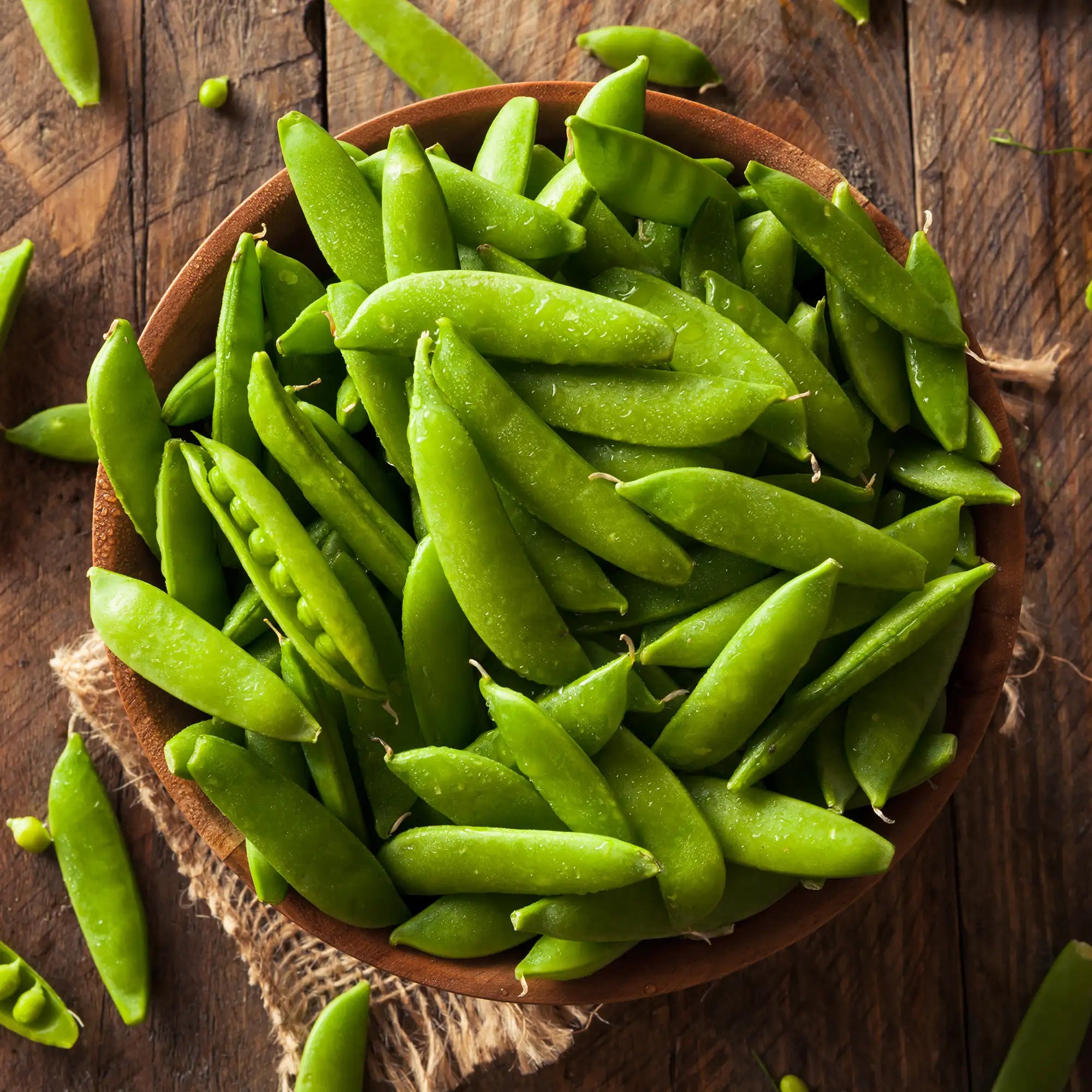 Wooden bowl filled with green sugar snap peas on a wooden table
