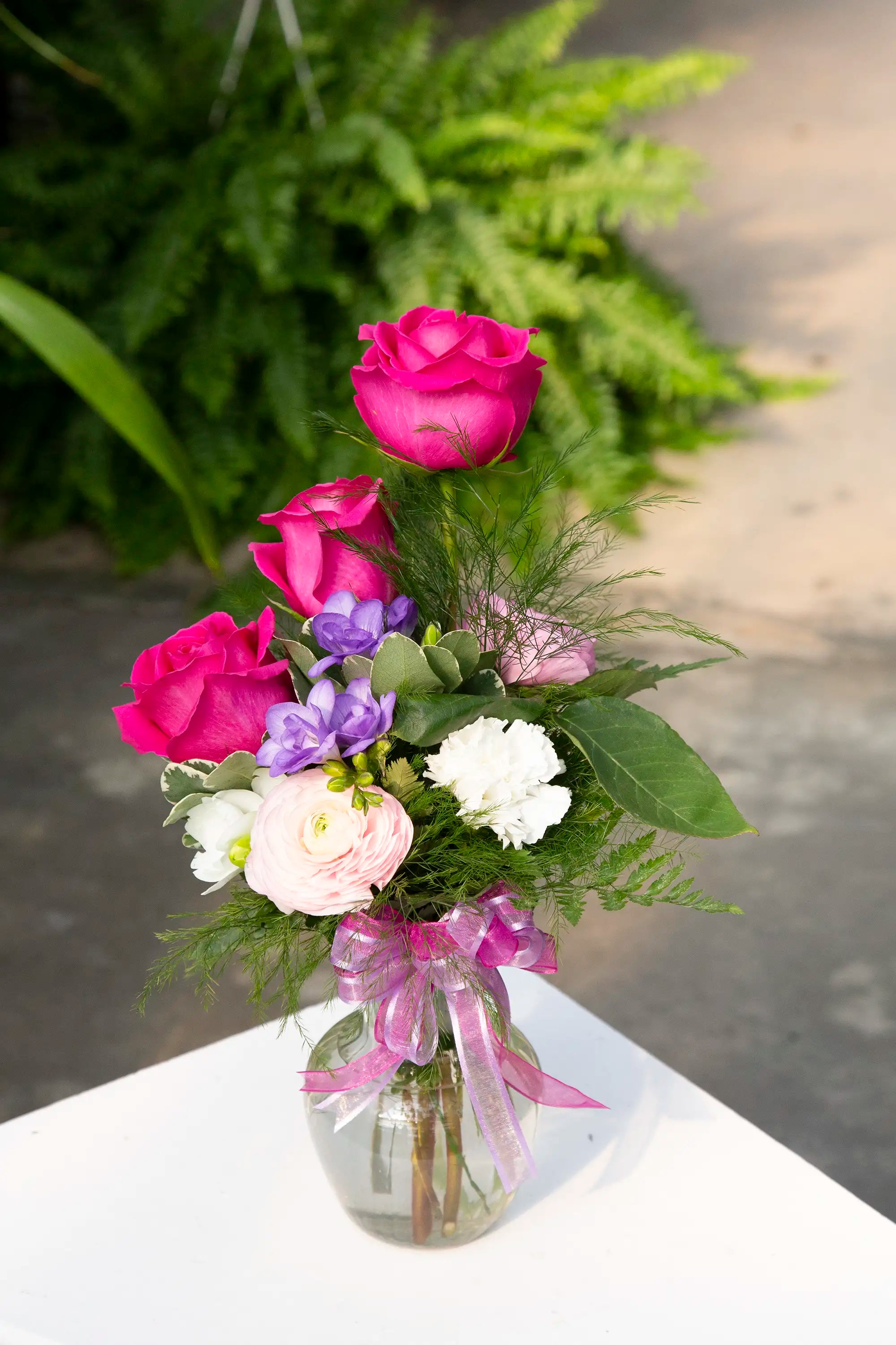 Bouquet of flowers in a vase with a pink ribbon on a white surface.